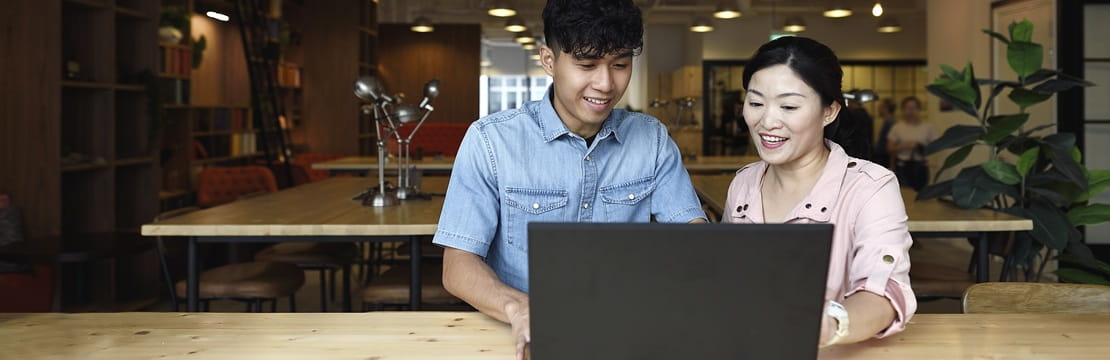 Parent and child sitting together at a laptop in a modern workspace, reviewing financial basics and discussing foundational investing concepts.